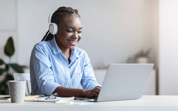 Fekete titkár dolgozik laptop és zenét hallgatni fülhallgató az irodában — Stock Fotó