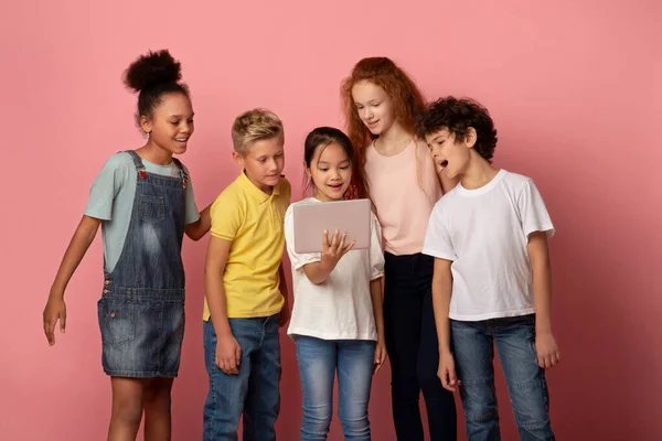 Educación en línea. Niños felices viendo interesante lección web en tableta sobre fondo rosa — Foto de Stock