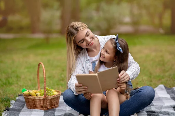 Lilla dottern läser bok med mor tillbringar helgen i parken — Stockfoto