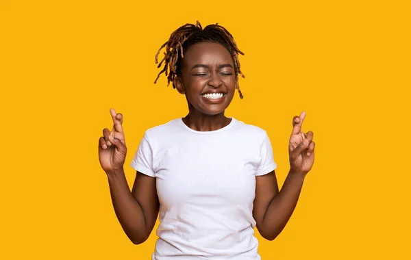 Молодая черная женщина закрывает глаза, скрещивает пальцы с надеждой — стоковое фото
