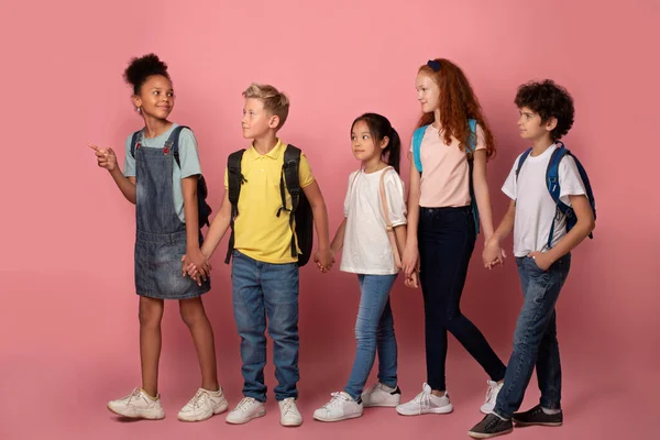 Körpergröße Porträt von Schulkindern, die Hand in Hand über rosa Hintergrund zur Schule gehen — Stockfoto