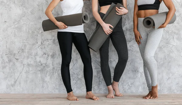 Подходящие женщины в спортивной одежде стоят с фитнес-коврики в руках у стены — стоковое фото