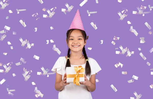 Mädchen mit Geburtstagsgeschenk steht unter fallendem Konfetti, lila Hintergrund — Stockfoto
