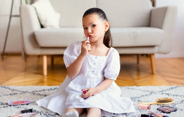 Niña poniéndose pintalabios jugando con las madres cosméticos en interiores — Foto de Stock