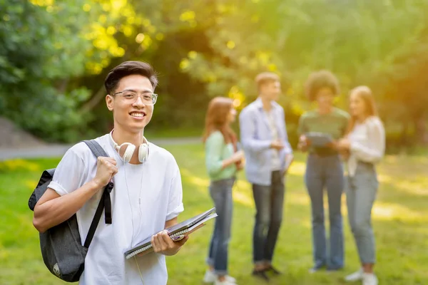 Programas de bolsas de estudo. Sorrindo masculino asiático estudante universitário com mochila e cadernos de trabalho ao ar livre — Fotografia de Stock