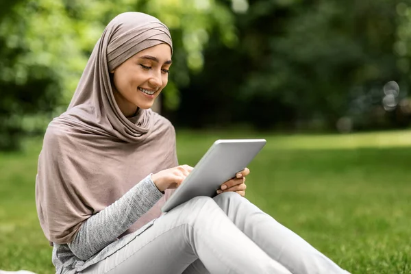 Mosolygós lány hidzsáb segítségével digitális tabletta, pihenés a parkban — Stock Fotó