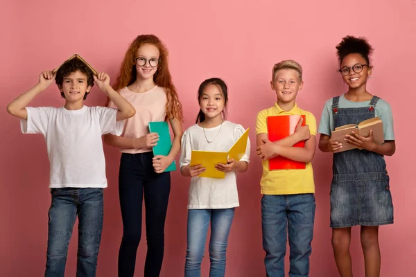 Багатонаціональна група дітей з книгами та блокнотами, готовими до школи на рожевому фоні студії — стокове фото