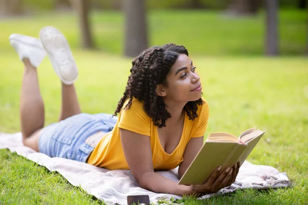 梦中的非洲裔美国女孩躺在带着书本的野餐毛毯上放松，外面 — 图库照片