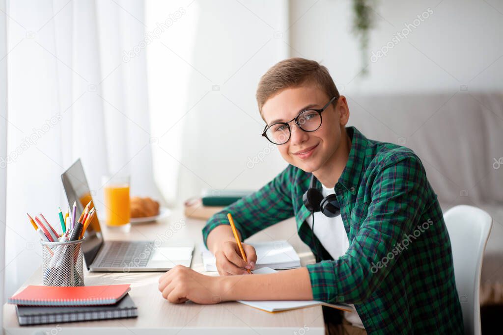 Happy teen guy doing homework at home