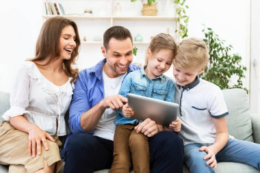 Ebeveynler ve çocuklar tabletleriyle oturup gülüyorlar.