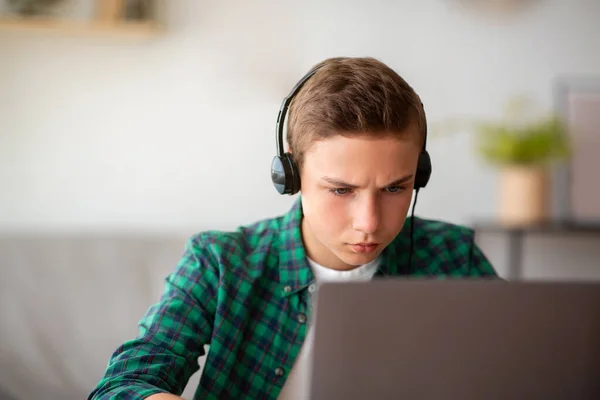 Сконцентрированный подросток с ноутбуком, сидит дома один — стоковое фото