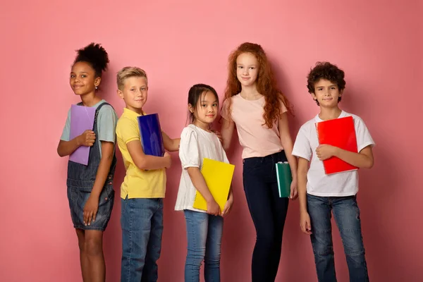 Bereit für die Schule. Multinationale Klassenkameraden halten Notizbücher über rosa Hintergrund — Stockfoto