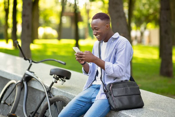Pozytywny czarny człowiek z rower pisanie wiadomości na komórkę w miejskim parku — Zdjęcie stockowe