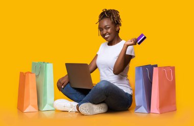 Bilgisayarı ve kredi kartını kullanarak online alışveriş yapan pozitif siyah bir kız.