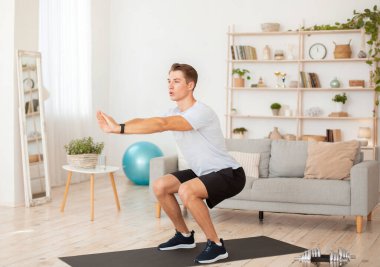 Evde formda kalıyor. Spor giyimli genç bir adam ve iç mekanda fitness takip cihazları var.