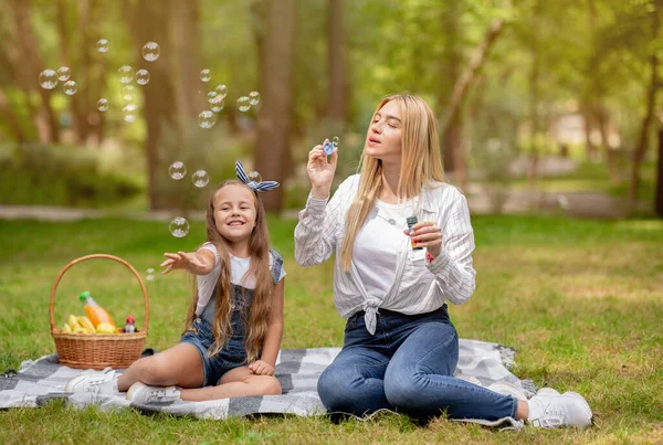 Mladá maminka a dcera foukání mýdlo bubliny v zeleném parku — Stock fotografie