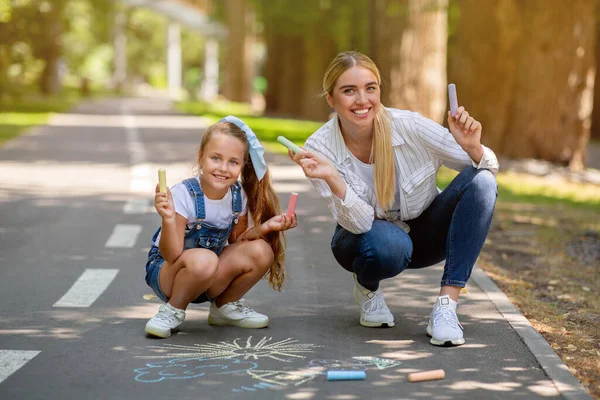 Lycklig mamma och dotter håller färgglada kritor Ritning i parken — Stockfoto