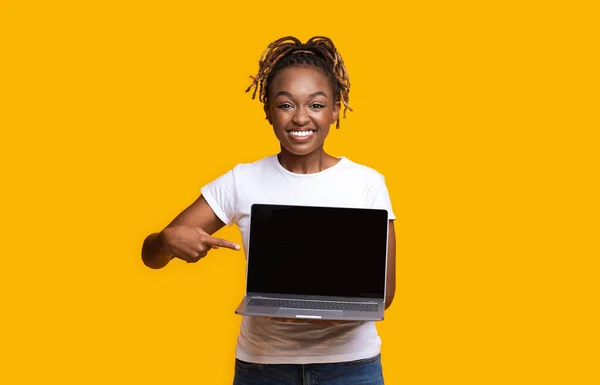 Chica africana apuntando a la pantalla del ordenador portátil en blanco sobre fondo amarillo — Foto de Stock
