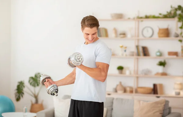 Treinamento de fisiculturista com halteres pesados em casa. Muscular cara olha para bíceps — Fotografia de Stock