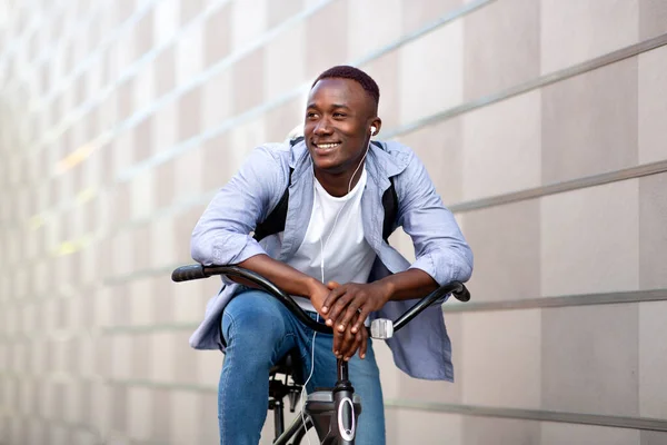 在市中心砖墙附近骑自行车的英俊黑人，背着背包和耳机 — 图库照片