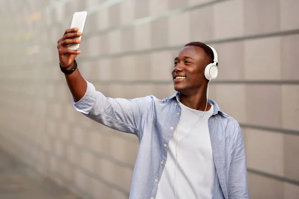 Велетенський афроамериканець у навушниках сідає на мобільний пристрій біля цегляної стіни. — стокове фото