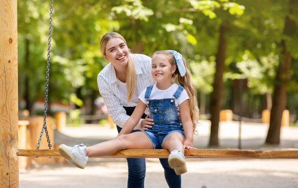Lycklig mor knuffar lilla dotter på gungor på utomhus lekplats — Stockfoto