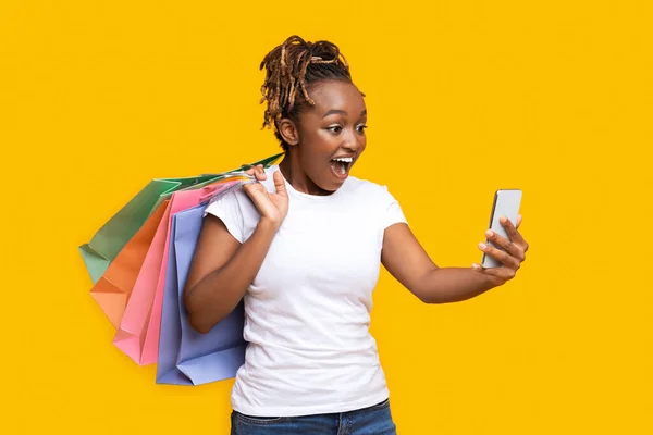 Eccitato ragazza africana con borse della spesa guardando lo schermo del telefono — Foto Stock