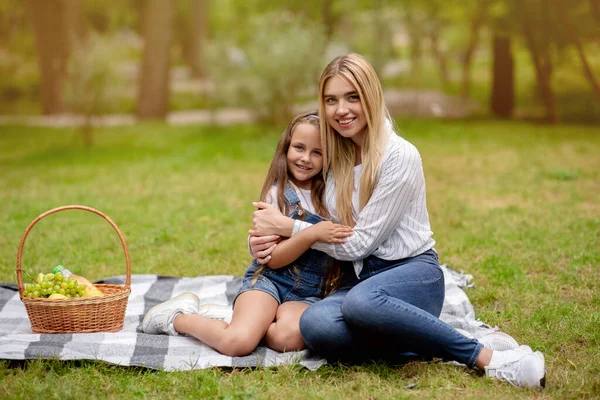 Liten flicka kramas med mor bindning på picknick utanför — Stockfoto