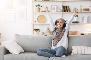 Aşırı neşeli Müslüman kız evde kablosuz kulaklıkla müzik dinliyor.