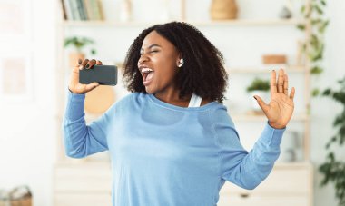 Akıllı telefonu mikrofon olarak kullanan Afro bir kadın.