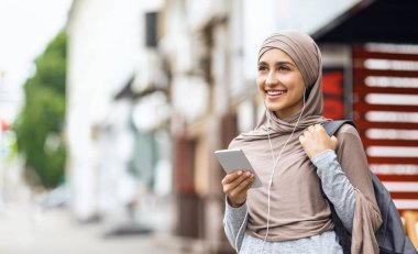 Kulaklık ve akıllı telefon kullanan tesettürlü pozitif kız.