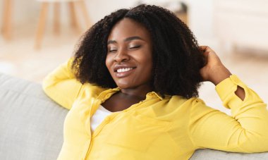 Afro kız evinde kanepede dinleniyor.