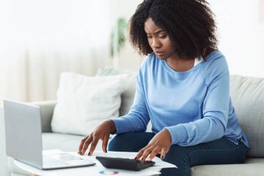 Evde hesap makinesi ve laptop kullanan bir kadın