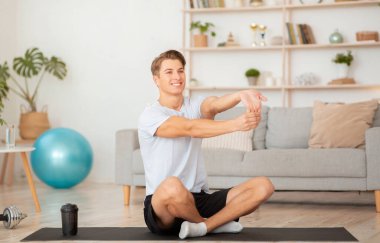Formda kalmak için ev sporları. Gülümseyen adam el egzersizi yapıyor, lotus pozisyonunda mindere oturuyor.