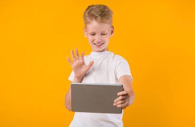 Mutlu çocuk video çağrısı ve el sallama için tablet kullanıyor.