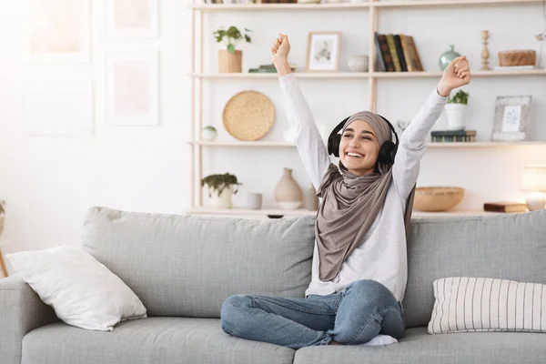 Joyed ragazza musulmana in hijab ascoltare musica in cuffie wireless a casa — Foto Stock