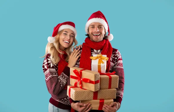 Портрет чарівної молодої пари в різдвяному вбранні, що тримає купу подарункових коробок на синьому фоні — стокове фото