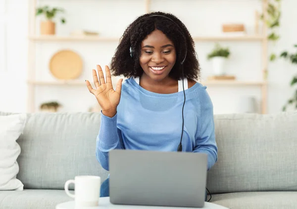 Sorridente signora nera seduta sul divano con auricolare — Foto Stock