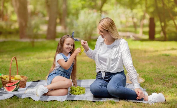 Mor och dotter äter druvor sitter på rutig i parken — Stockfoto