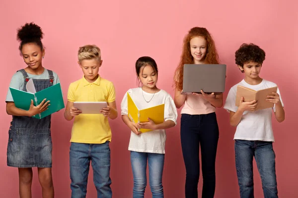 Цілеспрямовані молоді учні з блокнотами, книжками та гаджетами зосереджені на навчанні на рожевому фоні — стокове фото