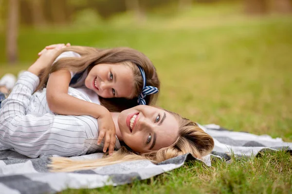 Aranyos anya és lánya ölelkezve fekszik a takarón a parkban. — Stock Fotó