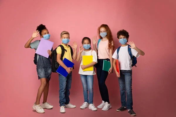 Освіта під час пандемії вірусу. Портрет школярів у медичних масках, що махають на рожевому фоні — стокове фото