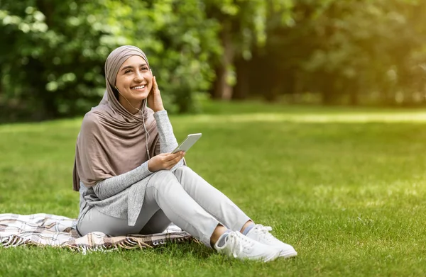 Chica musulmana alegre escuchando música, usando un teléfono inteligente —  Fotos de Stock