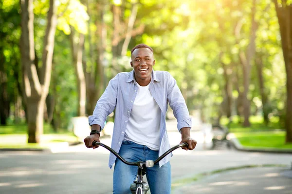 Sonriente chico negro disfrutando de su paseo en bicicleta en el parque en verano — Foto de Stock
