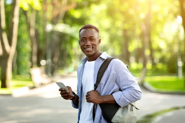 Happy czarny facet w casual strój za pomocą telefonu komórkowego podczas spaceru w parku miejskim — Zdjęcie stockowe