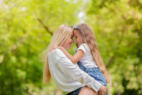 Schöne Mutter umarmt ihre Tochter, die das Wochenende im grünen Park verbringt — Stockfoto