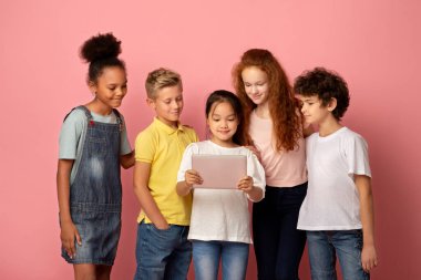 Çok uluslu genç öğrenciler pembe arka plan üzerinde birlikte çalışmak için tablet bilgisayar kullanıyorlar.