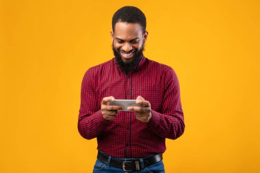 Sarı arka planda cep telefonu kullanan heyecanlı afro adam.