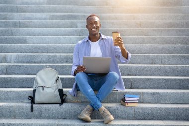 Çevrimiçi iletişim. Dışarıdaki merdivenlerde internetten biriyle konuşan Afro-Amerikalı genç bir adam.