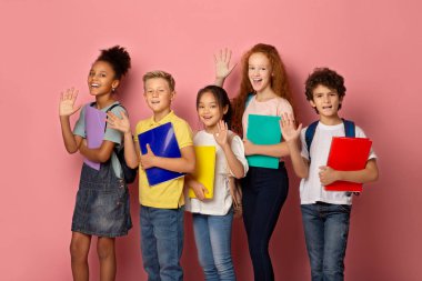 Okul çantalı ve pembe arka planda sallanan not defterli neşeli çocukların portresi.